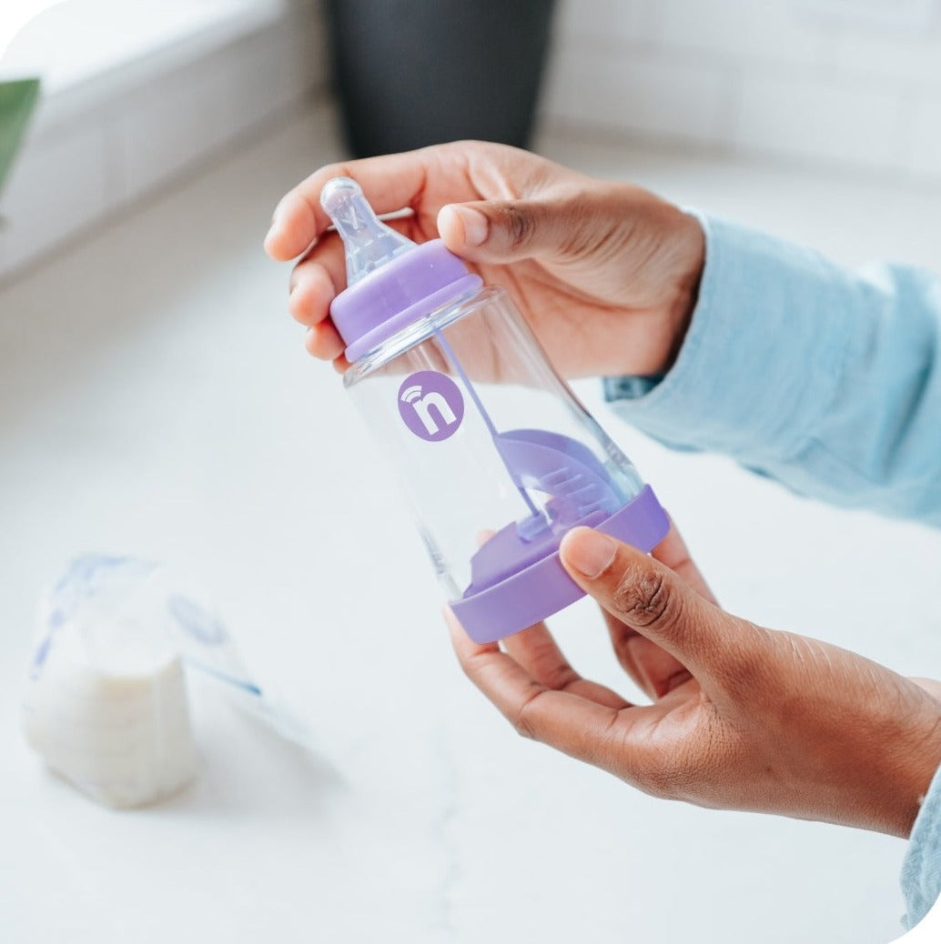The nfant® Smart Bottle is shown hold up by a parent assembling it before feeding a baby.